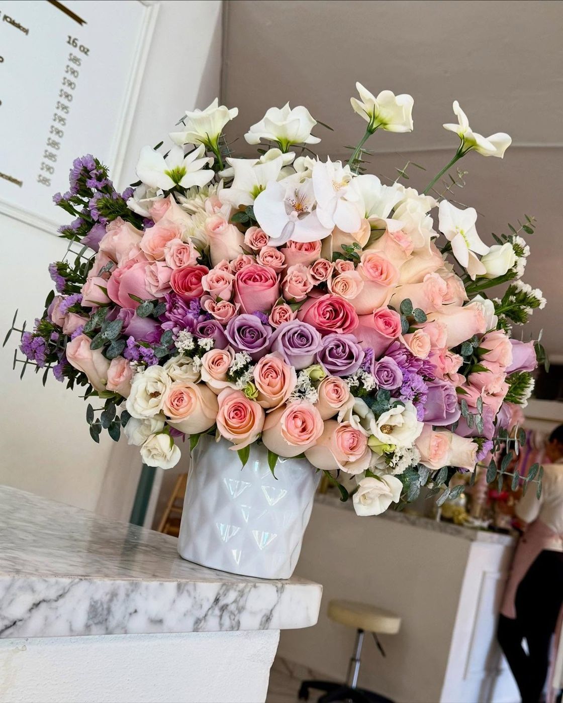 Arreglo de rosas rosas y lilas en la recepción de Lindas Café & Flores