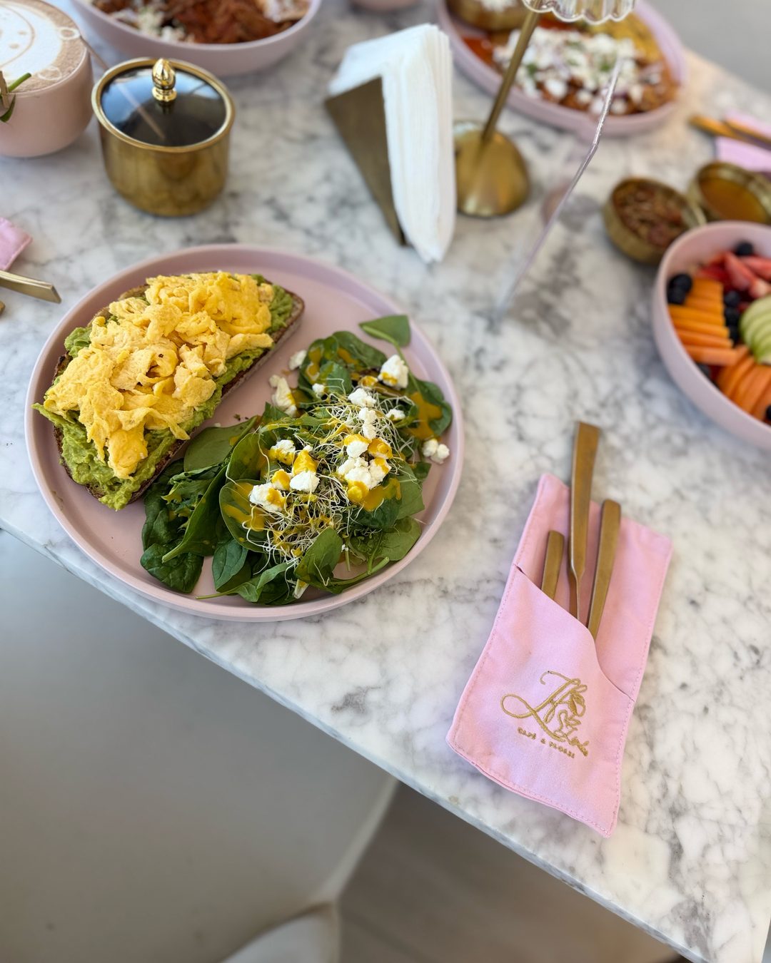 Avocado Toast con huevo revuelto y ensalada de espinaca en plato rosa, sobre mesa de mármol