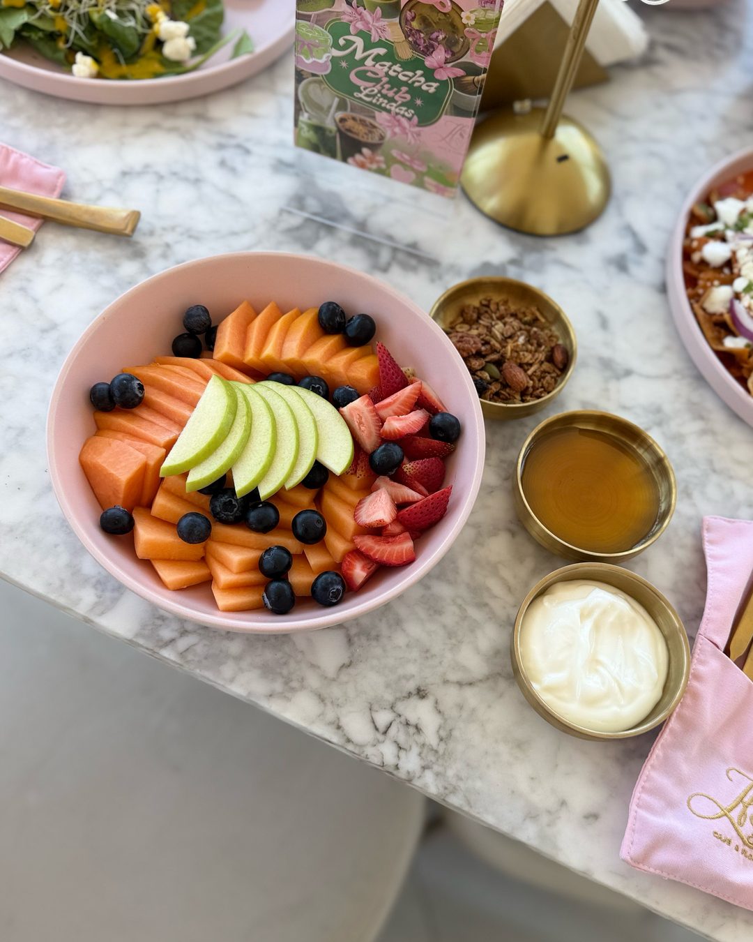 Bowl de fruta con papaya, manzana, fresas y moras azules, con toppings al lado