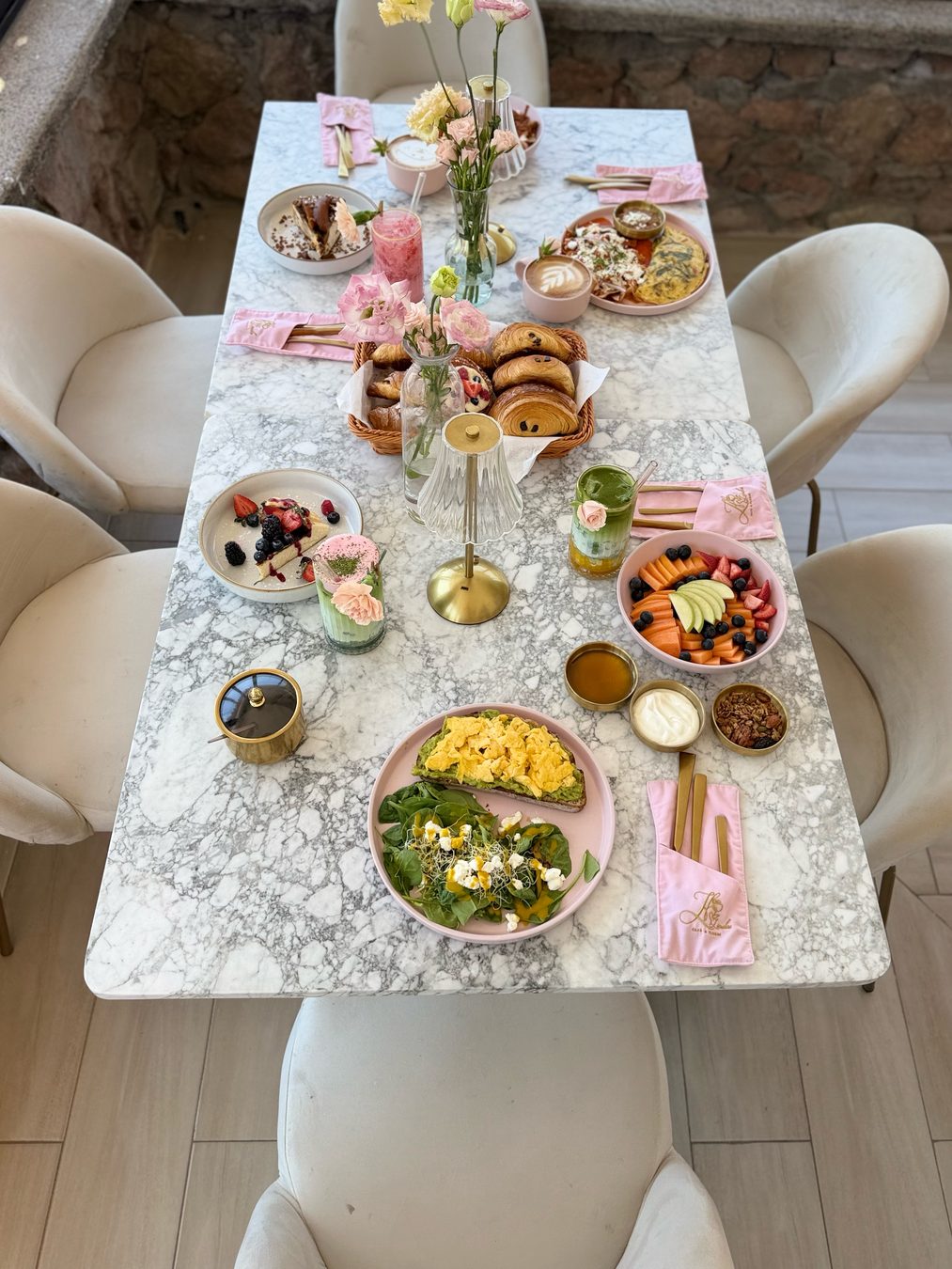 Mesa de mármol puesta para un brunch en grupo, con flores al centro y servilletas rosas de Lindas